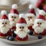 A festive platter of Cute Strawberry Santa Desserts, each made from strawberries, cream, and decorated with chocolate chips and coconut flakes.
