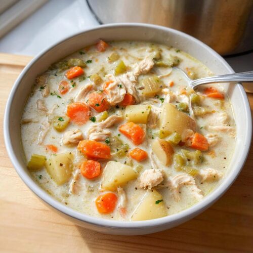A close-up of a bowl filled with Easy Creamy Chicken Soup, showing chunks of chicken, potatoes, carrots, and celery.