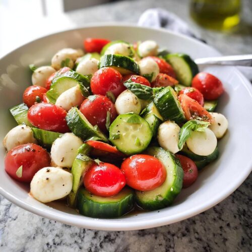 Close-up of a vibrant Easy Cucumber Caprese Salad featuring cherry tomatoes, mozzarella balls, and sliced cucumbers.