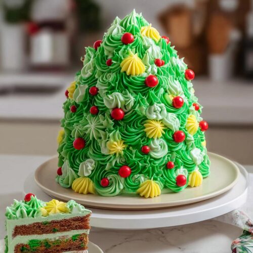 A beautifully decorated Festive Santa & Tree Cake, shaped like a Christmas tree with green frosting and red ornaments.