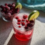 Close-up of a fizzy red Ginger Ale Christmas Punch garnished with cranberries and a lime slice.