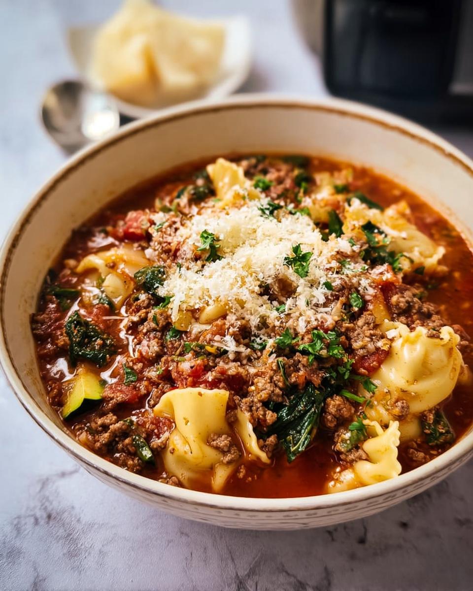 A close-up bowl of Healthy Crockpot Lasagna Soup featuring pasta, ground meat, vegetables, and topped with grated parmesan cheese.