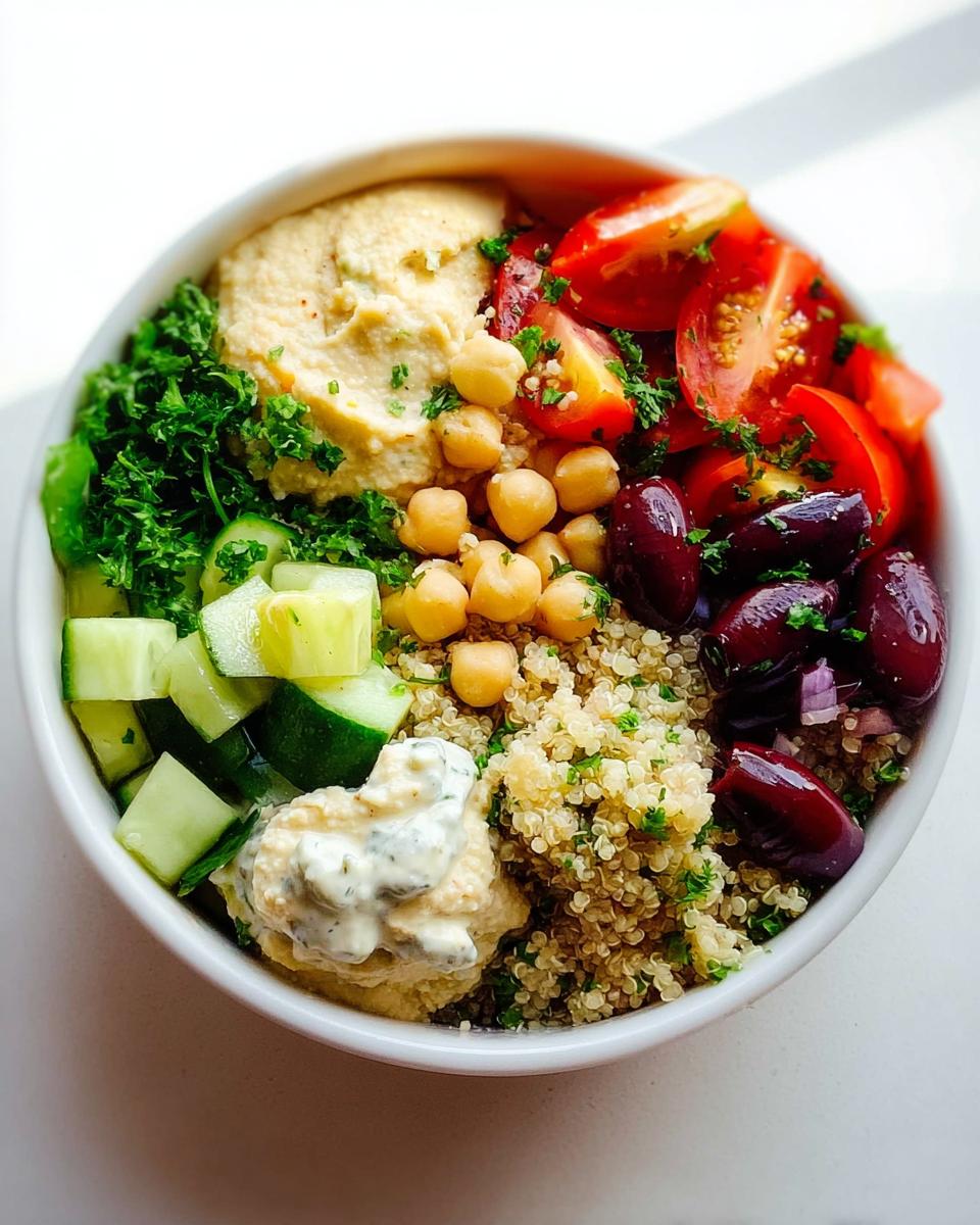 Overhead view of a bowl filled with ingredients for a Healthy Mediterranean Snack Box, including hummus, quinoa, olives, and cucumber.