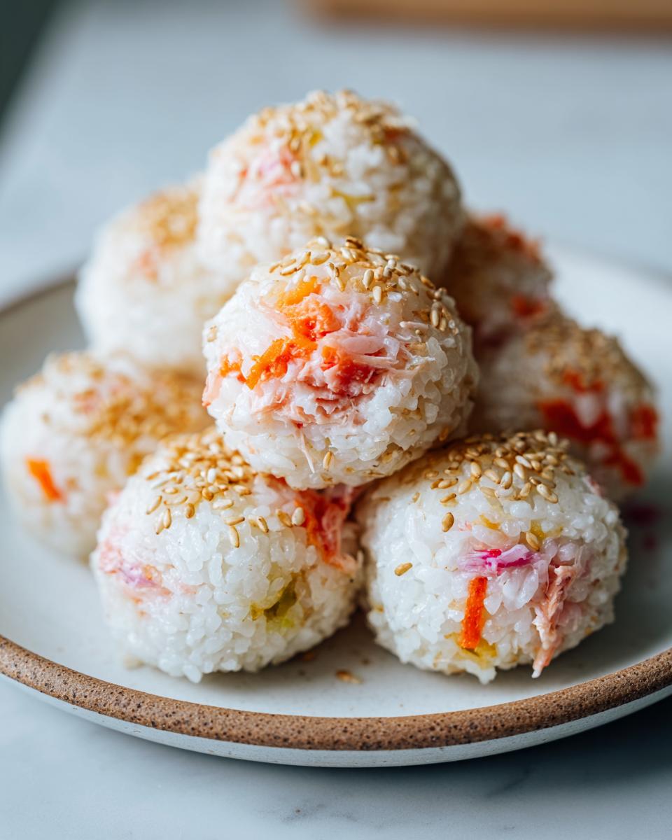 A stack of several Healthy Sushi Lunch Balls made with white rice and pink/orange filling, topped with toasted sesame seeds.