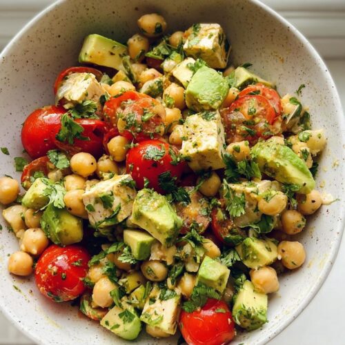 Overhead view of a bowl filled with High Protein Chickpea Salad, featuring chickpeas, avocado chunks, cherry tomatoes, and herbs.