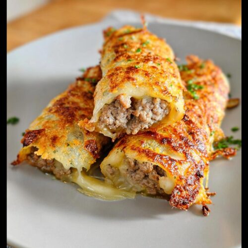 Three golden-brown Keto Philly Cheesesteak Roll Ups filled with seasoned ground meat and melted cheese, served on a white plate.
