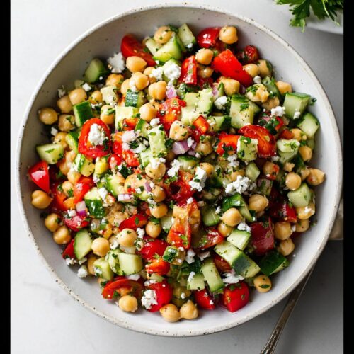 Overhead view of a fresh Mediterranean Chickpea Salad with cucumbers, tomatoes, feta, and herbs in a light bowl.