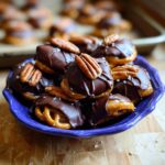 A pile of Pretzel Turtles Christmas Edition treats, covered in chocolate and topped with pecans and sea salt.