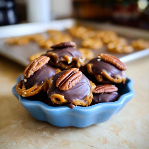 Close-up of Pretzel Turtles Christmas Edition candies in a blue bowl, topped with pecans.