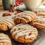 Close-up of several warm Spice Drop Cookies on a cooling rack, drizzled with a white glaze and studded with nuts.