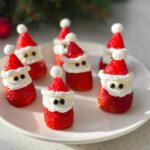 Adorable Strawberry Santas with whipped cream and black candy eyes arranged on a white plate.