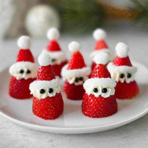 A festive plate of Strawberry Santas with whipped cream and black candy eyes, perfect for holiday treats.