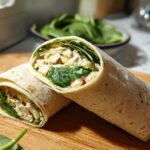 Two halves of a freshly made Chicken & Spinach Wrap, showing diced chicken and vibrant green spinach inside a tortilla.