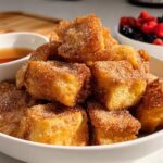 A close-up of golden Air Fryer Churro French Toast Bites coated in cinnamon sugar, served with syrup and berries.