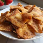 A close-up of crispy Air Fryer Cinnamon Sugar Tortilla Chips heavily coated in cinnamon and sugar, piled on a white plate.