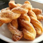 A pile of golden brown Air Fryer Cinnamon Twists heavily coated in sparkling cinnamon sugar on a white plate.