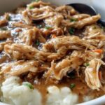 Close-up of shredded Asian Dump Chicken Crockpot served over creamy mashed potatoes with gravy and herbs.