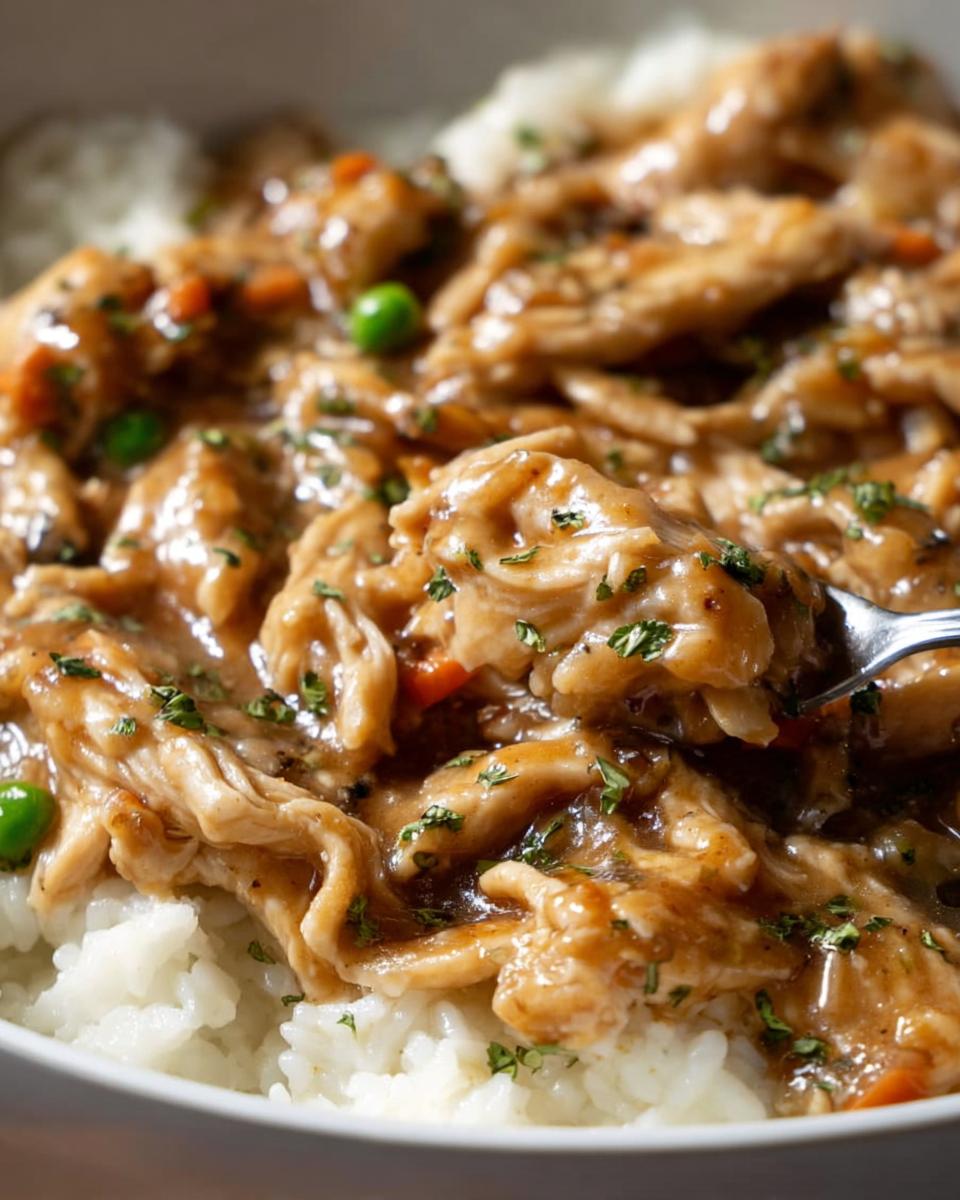 Close-up of shredded Asian Dump Chicken Crockpot in savory sauce served over white rice, garnished with peas and parsley.