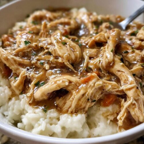 Close-up of shredded Asian Dump Chicken Crockpot served over a bed of white rice in a bowl.