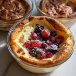 Three individual servings of baked Pancake Bowl You Bake in the Oven topped with mixed berries and powdered sugar.