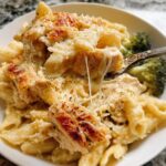 A spoonful of cheesy Baked Garlic Parm Chicken Pasta showing melted cheese strings, served with broccoli florets.