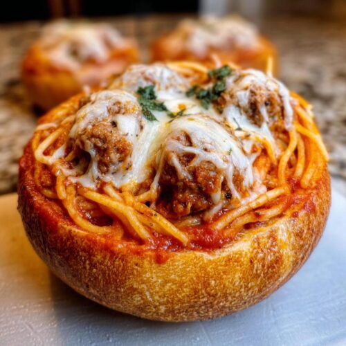 A close-up of a Baked Spaghetti with Italian Sausage Bread Bowl topped with melted mozzarella cheese and parsley.