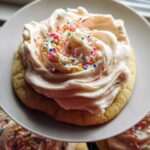 Close-up of a sugar cookie topped with thick, swirled Bakery-Style Sugar Cookie Frosting and colorful sprinkles.
