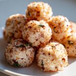 A close-up stack of perfectly formed, seasoned Bento Box Sushi Balls on a white plate.