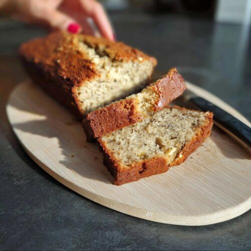 Two slices of moist Best Ever Sour Cream Banana Bread on a wooden board, with the rest of the loaf visible.