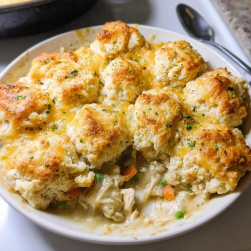 A close-up of a bowl of Cheddar Biscuit Chicken Pot Pie, showing fluffy biscuits topped with melted cheese over creamy chicken and vegetables.