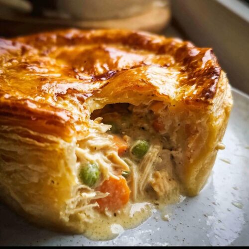 Close-up of a single-serving Chicken Pot Pie with Puff Pastry, showing the creamy filling oozing out.