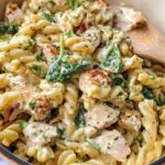 Close-up of creamy Chicken Spinach Protein Pasta with fusilli, chicken pieces, and wilted spinach.