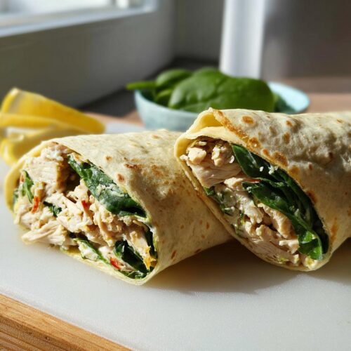 A halved Chicken & Spinach Wrap showing shredded chicken, fresh spinach, and creamy filling inside a warm tortilla.