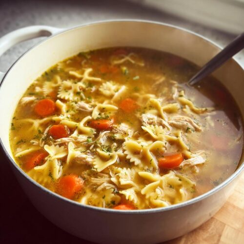 Close-up of a pot filled with rich Chicken & Turkey Soup featuring bowtie pasta, sliced carrots, and shredded meat.