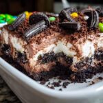 A rich slice of Chocolate Pudding Dirt Cake showing layers of crushed cookies, cream, and chocolate pudding topping.