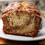 Close-up of a thick slice cut from a Cinnamon Banana Brunch Loaf, showing a moist crumb and cinnamon swirl, topped with a light glaze.