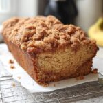 A freshly baked loaf of Cinnamon Crunch Banana Bread cooling on a wire rack with a thick, sugary cinnamon streusel topping.