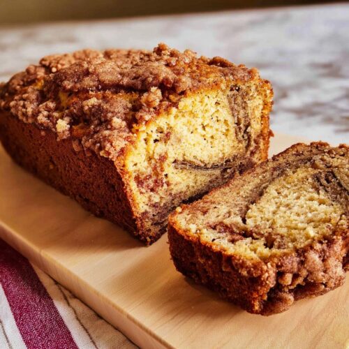 A loaf of Cinnamon Streusel Banana Bread, partially sliced, showing the moist interior and crumb topping.