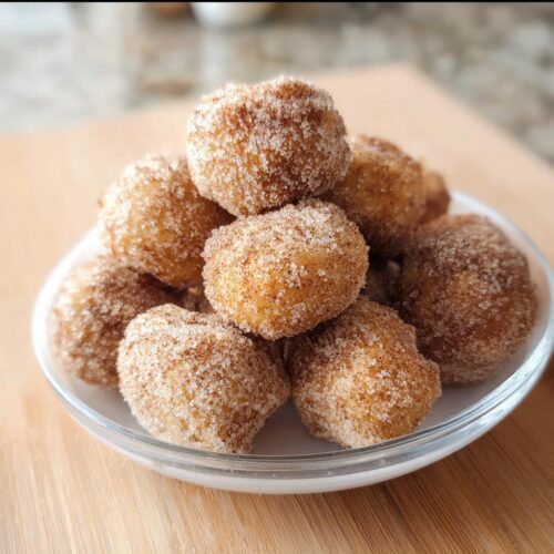 A close-up of several golden Cinnamon Sugar Air Fryer Donut Holes piled high in a clear glass bowl.