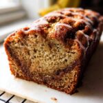 Close-up of a loaf of Cinnamon Swirl Banana Bread, showing the moist crumb and cinnamon layer, drizzled with white icing.