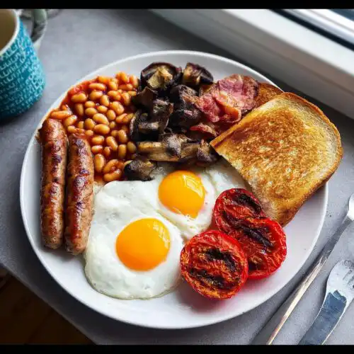A plate featuring a Classic British Breakfast at Home with sausages, eggs, bacon, beans, mushrooms, toast, and grilled tomatoes.