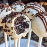 A close-up of several white chocolate coated Cookies & Cream Cake Pops, one showing the dark chocolate cake interior.