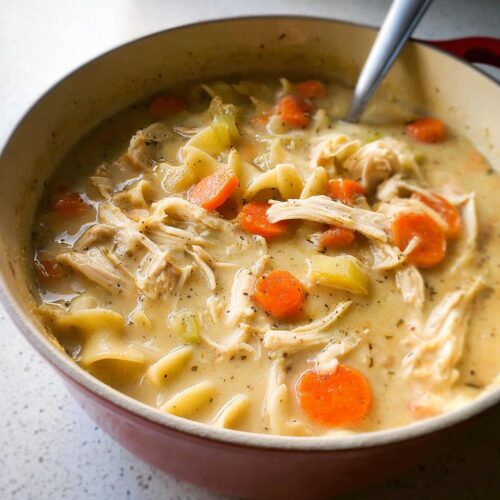 A close-up of rich Creamy Chicken Noodle Soup for Dinner, featuring shredded chicken, egg noodles, and bright carrots in a thick broth.