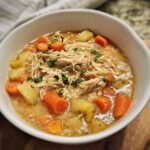 A close-up of a white bowl filled with Creamy Slow Cooker Chicken Soup featuring shredded chicken, carrots, and potatoes.