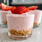 Three individual servings of Creamy Strawberry Mousse Cups layered over a graham cracker crust, topped with fresh strawberry slices.
