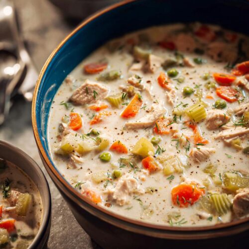 Close-up of a large bowl filled with thick, creamy turkey soup loaded with chunks of turkey, carrots, celery, and peas.