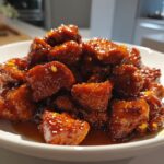 Close-up of sticky, glazed pieces of Crockpot Honey Soy Chicken piled high on a white plate.