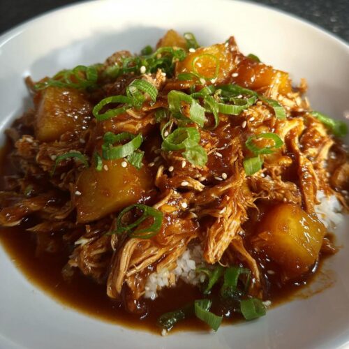 Close-up of shredded Crockpot Pineapple Teriyaki Chicken served over white rice, topped with pineapple chunks, green onions, and sesame seeds.