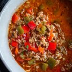 A close-up view of a bowl filled with rich, red Crockpot Stuffed Pepper Soup featuring ground meat, rice, and diced red and green peppers.