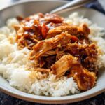 A bowl of shredded Crockpot Teriyaki Chicken served over fluffy white rice, coated in a glossy sauce.